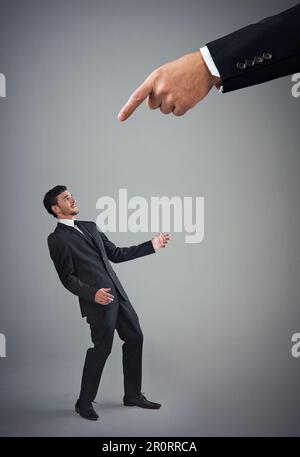 Know your place. Studio shot of a young businessman being reprimanded by a giant hand against a gray background. Stock Photo