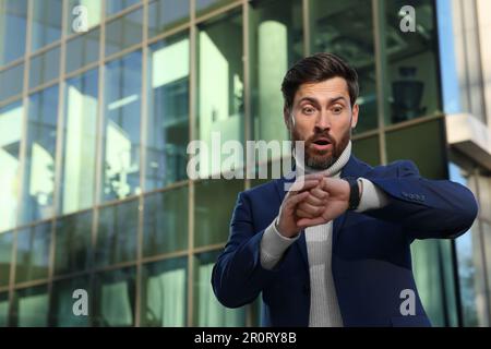 Surprised businessman checking time on watch near building. Being late concept Stock Photo