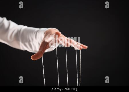 Woman pulling strings of puppet on black background, closeup Stock Photo