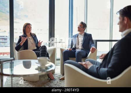 Working through things like a team. three businesspeople talking in a corporate office. Stock Photo