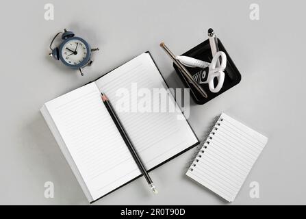 Stationery holder, notebooks and alarm on grey background Stock Photo