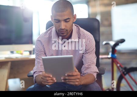 Focused on his online project. a designer using a digital tablet while working in an office. Stock Photo