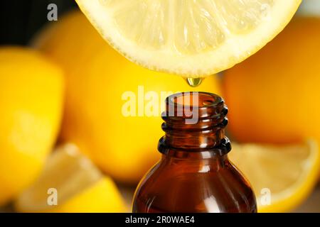 Dripping essential oil from lemon into bottle on blurred background, closeup Stock Photo