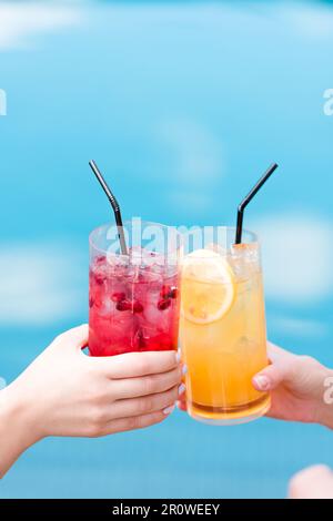 Women clinking glasses of cocktails in front of swimming pool Stock Photo