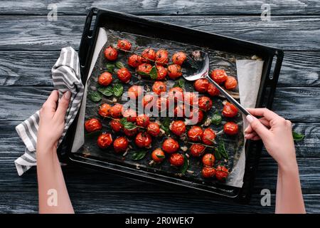 Woman pouring sauce on baked tomatoes in pan on dark wooden table Stock Photo