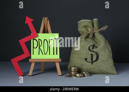 Economic profit. Money bag, arrow, coins and easel with note on grey table Stock Photo