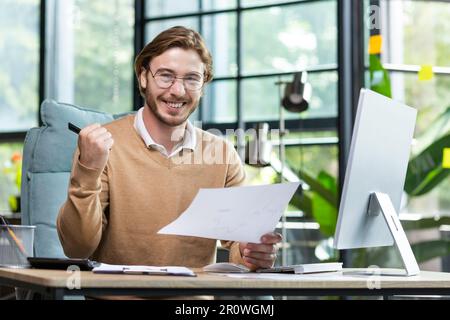 Portrait happy businessman financier, man with breed looking at camera and smiling, holding report with good achievement results and financial indicators celebrating victory, triumph gesture. Stock Photo