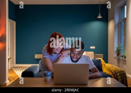 Happy couple reading good news in email on laptop. Glad smiling woman and man show video together Stock Photo