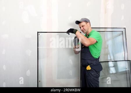 Worker in uniform preparing double glazing window for installation indoors Stock Photo