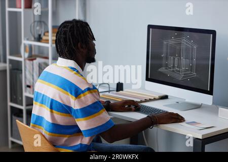 African American designer sitting at table in front of monitor and drawing blueprint on computer Stock Photo