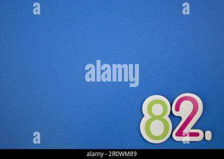 The number 82, placed on the edge of a blue background, photographed from above, colored green and red. Stock Photo