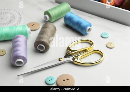 Sewing threads, scissors and buttons on white marble table Stock Photo