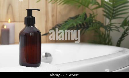 Black bottle of bubble bath and candles on tub indoors, space for text Stock Photo