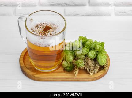 Mug with beer, fresh hops and ears of wheat on white wooden table Stock Photo