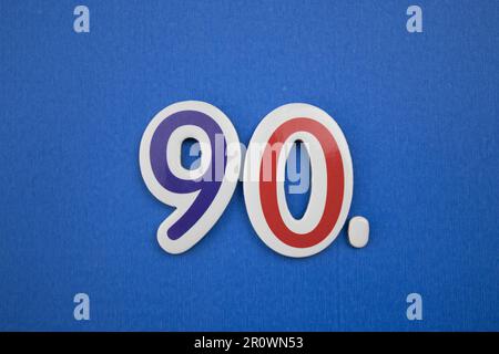 The number 90, placed on a blue background, photographed from above, colored light blue and red. Stock Photo