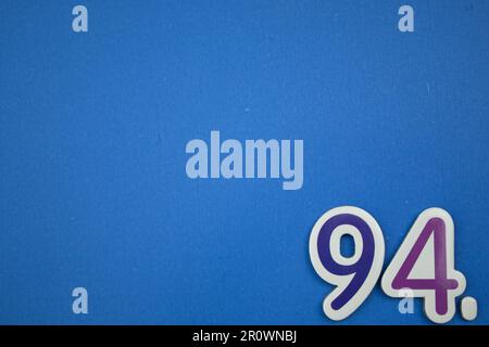 The number 94, placed on the edge of a blue background, photographed from above, colored blue and purple. Stock Photo