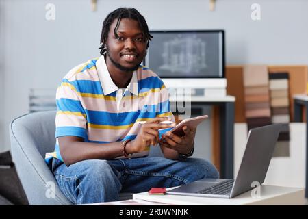 Portrait of African American designer smiling at camera while using tablet pc in his work Stock Photo