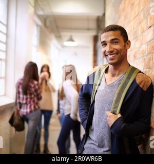 Mr Cool on campus. Portrait of a handsome young male student leaning against a wall with his friends in the background. Stock Photo
