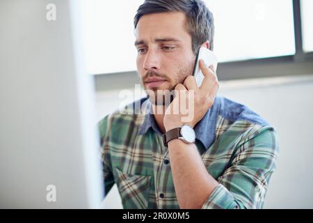 Im looking at the designs right now. a young designer talking on a cellphone while working on a computer. Stock Photo