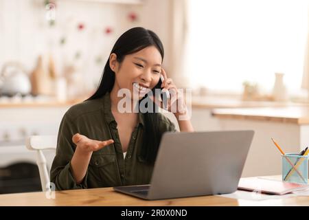 Beautiful chinese lady have phone conversation with client, kitchen interior Stock Photo