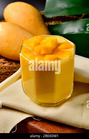 Refreshing Thai mango smoothie on wooden table and mangoes.Barracuda mango.Nam Dork Mai.Summer Drinks.Tropical Style.Food and drink concept. Stock Photo