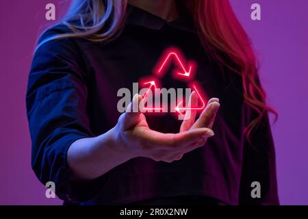 Woman holding virtual, digital, neon colored symbol of recycling. Modern technologies in global business sphere Stock Photo