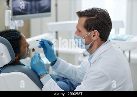 Side view portrait of male dentist wearing mask while working with child patient in clinic Stock Photo