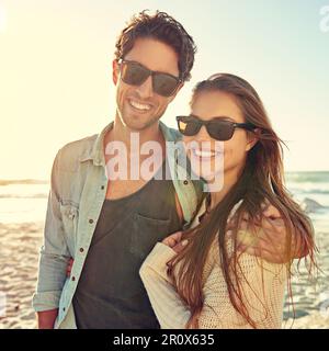 Enjoying a lazy afternoon at the beach. Portrait of a loving young couple wearing sunglasses standing together on the beach. Stock Photo