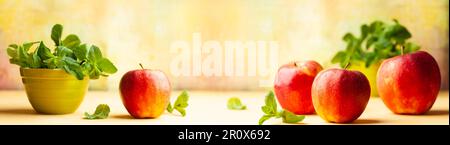 Still life with red apples and fresh mint in bowl on yellow background. Front view, copy space. Stock Photo