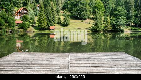 Wooden board, empty in front of blurred lake and house in forest. Perspective brown wood over blur in outdoor - can be used for display or montage Stock Photo