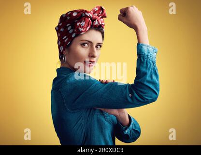 Woman, strong and flexing muscle portrait of a pinup girl in studio for beauty, power and fashion. Female person show bicep on a yellow background for Stock Photo