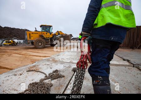 Ust-Luga, Leningrad oblast, Russia - November 16, 2021: Concrete road construction. Worker install concrete plates using metal hook with chain. No fac Stock Photo