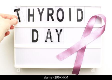 the inscription international thyroid day, violet ribbon and womans hand holding a letter on white background Stock Photo