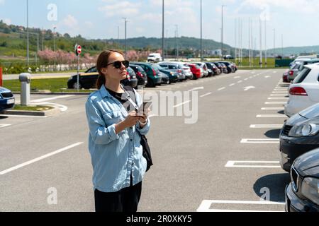 Woman using her mobile phone while standing on car parking. Stock Photo