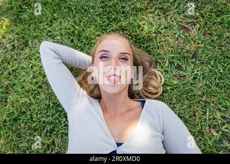 A girl lying on a meadow with an amused expression sticks her tongue out Stock Photo