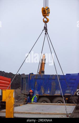 Ust-Luga, Leningrad oblast, Russia - November 16, 2021: Lifting concrete plate with mobile crane. Worker operator is out of focus Stock Photo