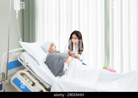 Indian daughter visit her elderly mother cancer patient undergoing course of chemotherapy in hospital. Woman holding hand of senior lady at clinic. he Stock Photo