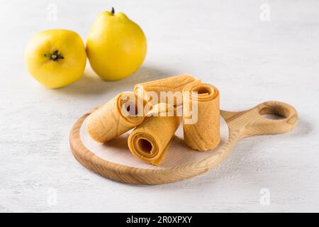 Natural quince pastille on a wooden board surrounded by fresh quince fruits on a light gray background Stock Photo