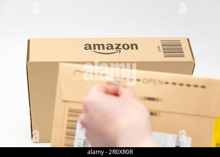 Fuji City, Shizuoka-Ken, Japan - March 26, 2023: Hand opening delivery envelope with selective focus on Amazon logo on cardboard box in background. Stock Photo