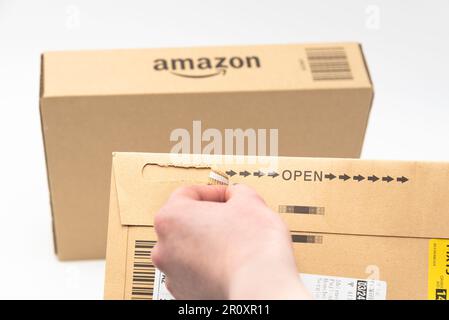 Fuji City, Shizuoka-Ken, Japan - March 26, 2023: Hand opening delivery envelope with cardboard box with Amazon logo slightly blurred in background. Stock Photo
