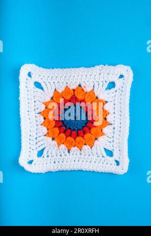 White granny square with central orange, red and blue concentric circle pattern, all on a Kingfisher blue background. Copy space top and bottom. Stock Photo