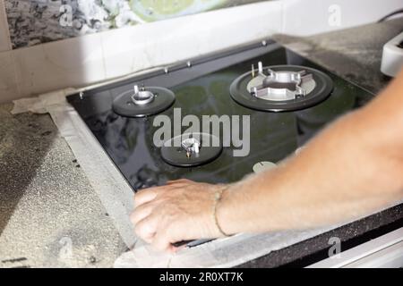 A man installs a built-in glass-ceramic gas stove on a kitchen countertop. Stock Photo