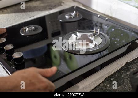 A man installs a built-in glass-ceramic gas stove on a kitchen countertop. Stock Photo