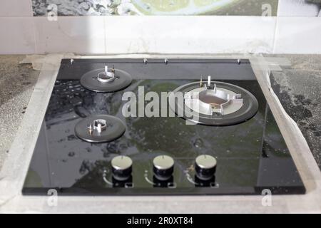 The black glass-ceramic gas hob is built into the kitchen worktop. Installation of a built-in stove. Stock Photo