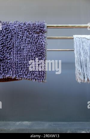 The cleaning foot scraper and mop cloth are hanging on the metal line after washing near the house wall, front view with the copy space Stock Photo