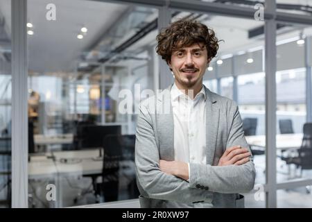 Portrait of successful young boss, businessman in business suit looking at camera and smiling, man with crossed arms working inside modern office building. Stock Photo