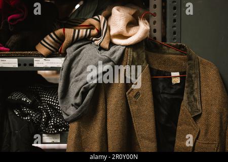 Madrid, Spain. May 1, 2022 An old brown wool jacket hangs on a rack in a secondhand clothing warehouse. Humanitarian aid distribution point for refuge Stock Photo