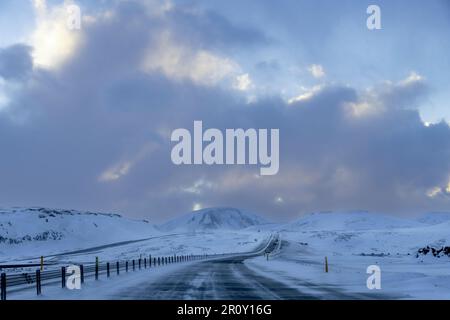 Driver’s perspective view over the almost empty ring road route 1 of Iceland bending through a snowy mountainous landscape and road recently cleared Stock Photo
