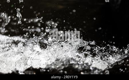 Close focus on fast moving water in river with stopped motion technique on dark background. Stock Photo