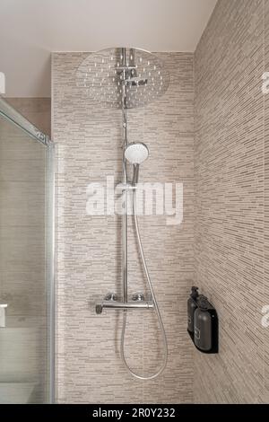 Close-up of a shower cabin with modern fixtures and glass doors and beige tiles in a cozy stylish compact bathroom. Concept shower room for young Stock Photo